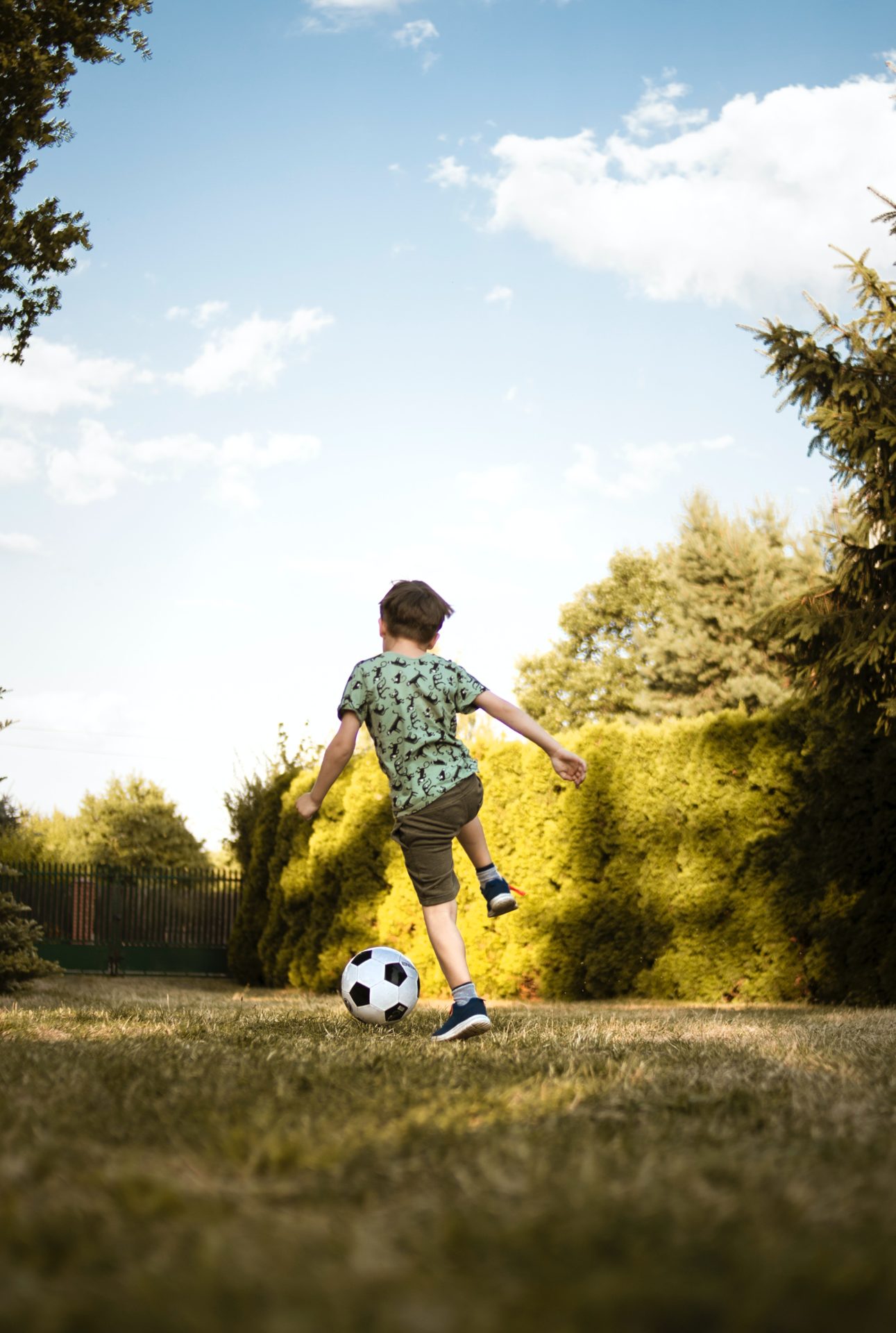 Kind auf der Wiese mit dem Rücken zur Kamera spielt vergnügt Fußball