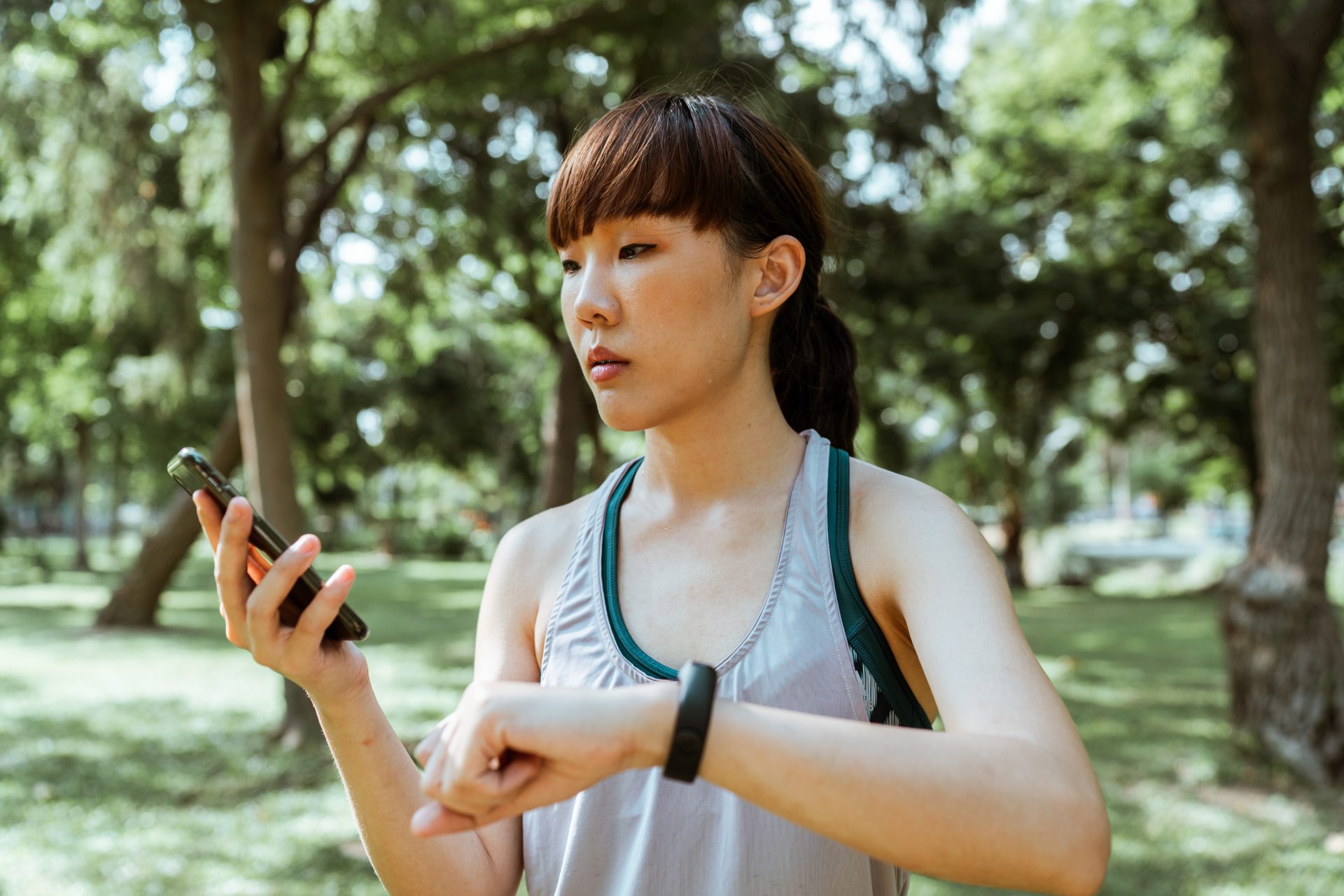 Eine Frau, die vermutlich gerade Cardio-Training in der Natur macht, vergleicht Ergebnisse auf Smartphone und Smartwatch